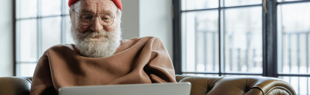 Älterer Mann sitzt auf dem Sofa und arbeitet am Laptop