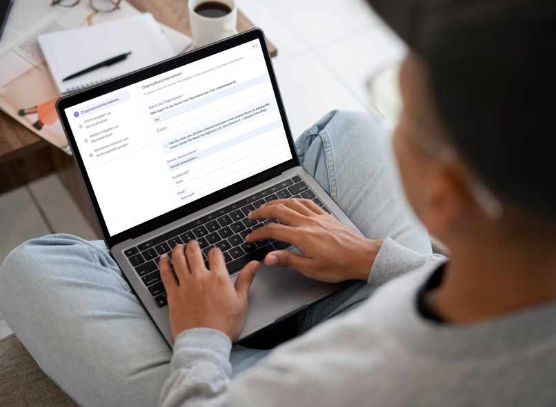 Mann mit Kappe und Brille sitzt im Schneidersitz vor seinem Laptop und gibt etwas ein